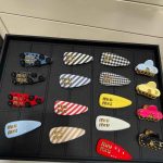 Assorted Miu Miu hair clips in red, black, gold, white, and green with bold branding – fashion accessory set