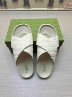 White Gucci cross strap slides for men with embossed GG logo – luxury summer footwear on a green designer box.